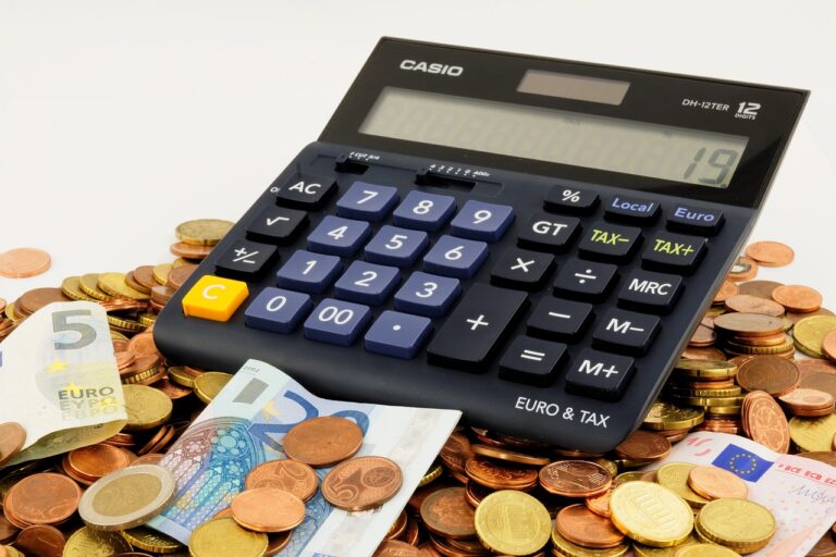 A imagem mostra uma calculadora sobre uma grande quantidade de moedas e cédulas de euro, sugerindo uma análise financeira, impostos ou cálculos de valores. Esse cenário pode estar relacionado a questões econômicas, como indenizações e compensações financeiras. Os **impactos da desapropriação** podem envolver cálculos complexos para determinar valores justos de compensação, levando em conta fatores como valorização do imóvel e prejuízos para os proprietários.