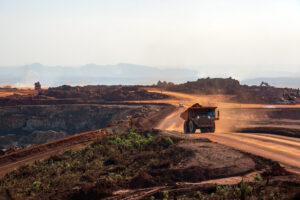 Direitos dos atingidos são o foco desta imagem, que revela uma extensa área de mineração a céu aberto, marcada por poeira, solo degradado e intensa movimentação de caminhões. O cenário evidencia os impactos sociais e ambientais que recaem sobre comunidades próximas — perda de território, contaminação da água, ruptura de modos de vida e risco à saúde. A foto reforça a urgência de garantir reparação integral, participação efetiva e justiça socioambiental, assegurando que o progresso econômico não se sobreponha aos direitos humanos.